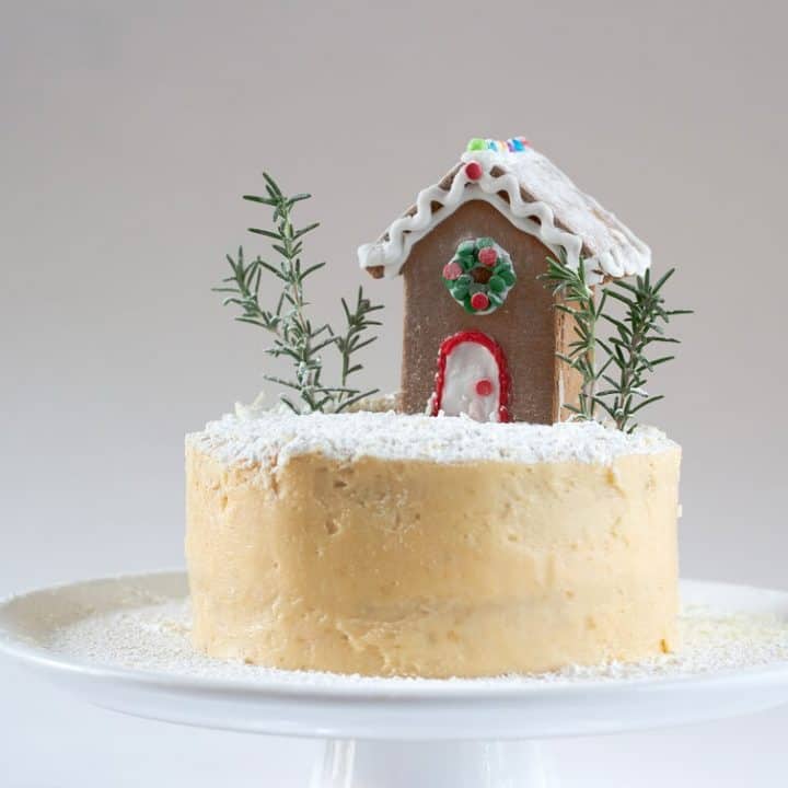 This white peppermint cake is decorated with a mini gingerbread house, rosemary sprigs, ground coconut and powdered sugar, but you can do whatever you like. #peppermint #layercake #swissmeringuebuttercream #dessert #gingerbreadhouse