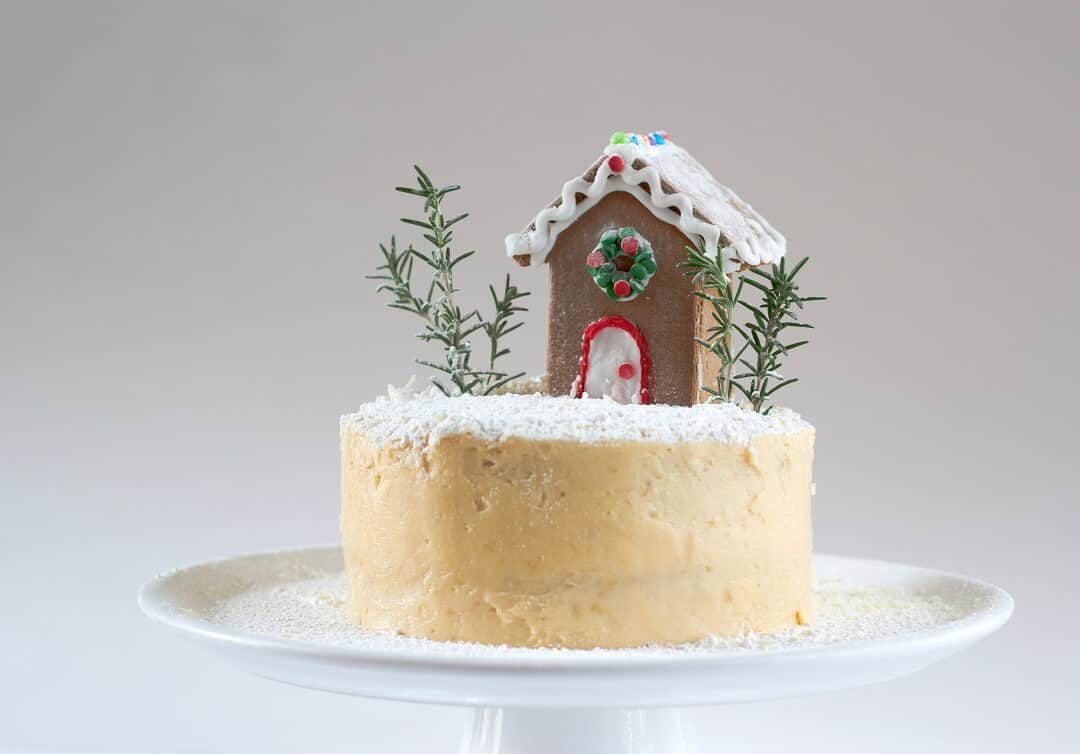 This white peppermint cake is decorated with a mini gingerbread house, rosemary sprigs, ground coconut and powdered sugar, but you can do whatever you like. #peppermint #layercake #swissmeringuebuttercream #dessert #gingerbreadhouse