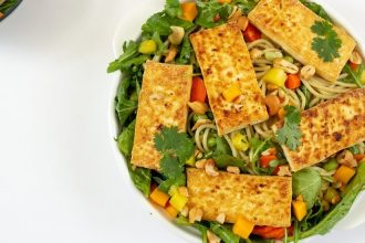 Bowl of pasta and arugula, topped with pan-fried tofu slabs.