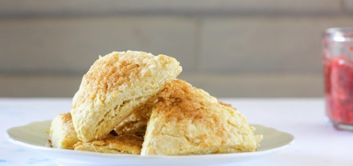 Stack of orange rosewater scones in front of a white brick wall.