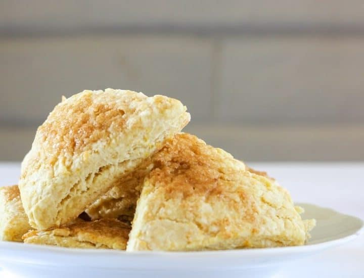 Stack of orange rosewater scones in front of a white brick wall.