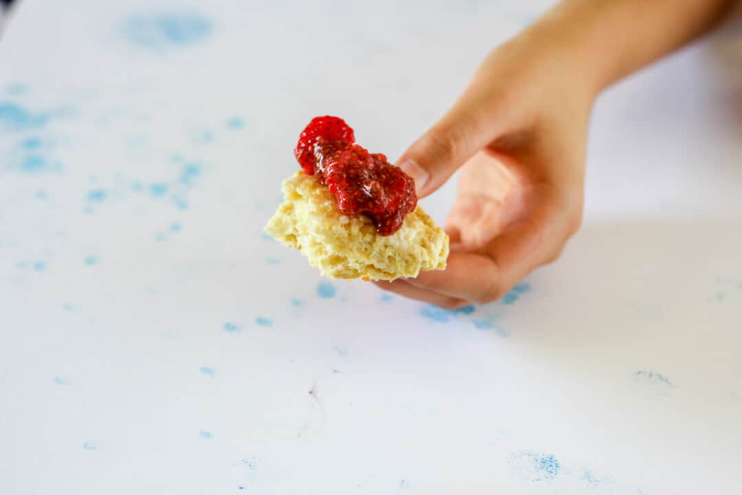 Torn bite of orange rosewater scone topped with strawberry chia compote.