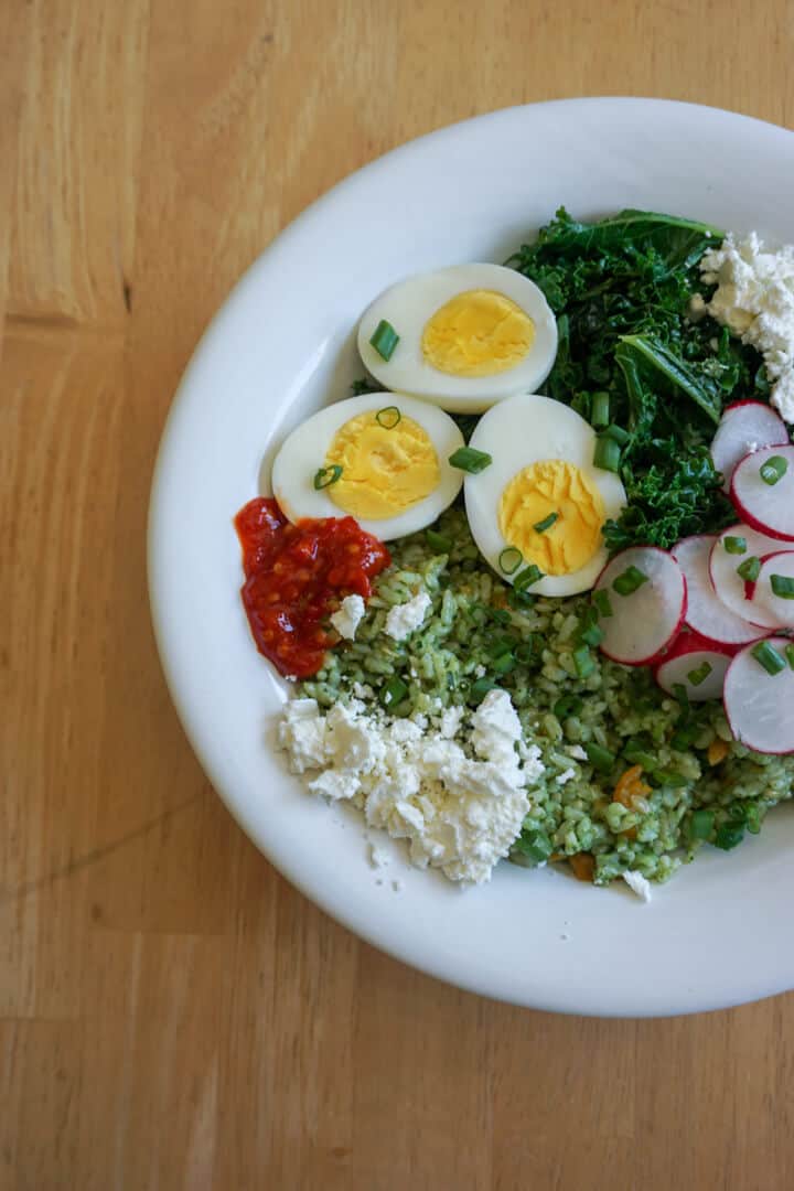 A citrus kale pesto rice bowl, topped with crumbled feta, hardboiled eggs, hot sauce and radishes.