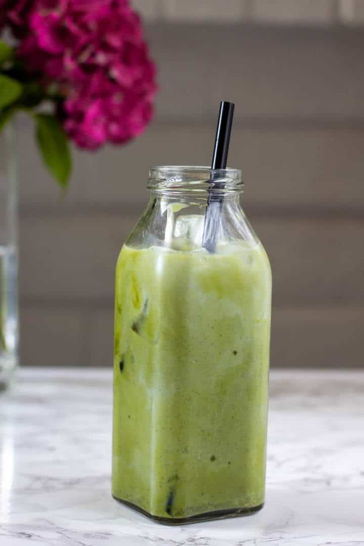 Tall glass bottle filled with creamy green matcha latte and a black straw.
