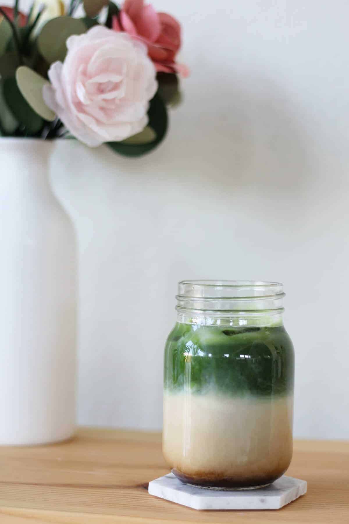 Glass filled with ice chunks, a shot of espresso, creamy milk and matcha.