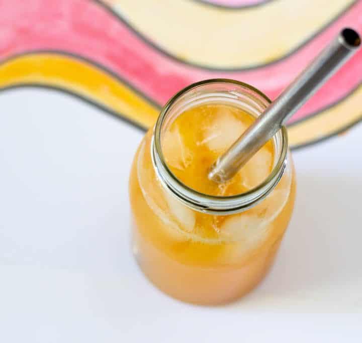 Glass jar filled with ice cubes and orange-y loquat lemonade and a metal straw.