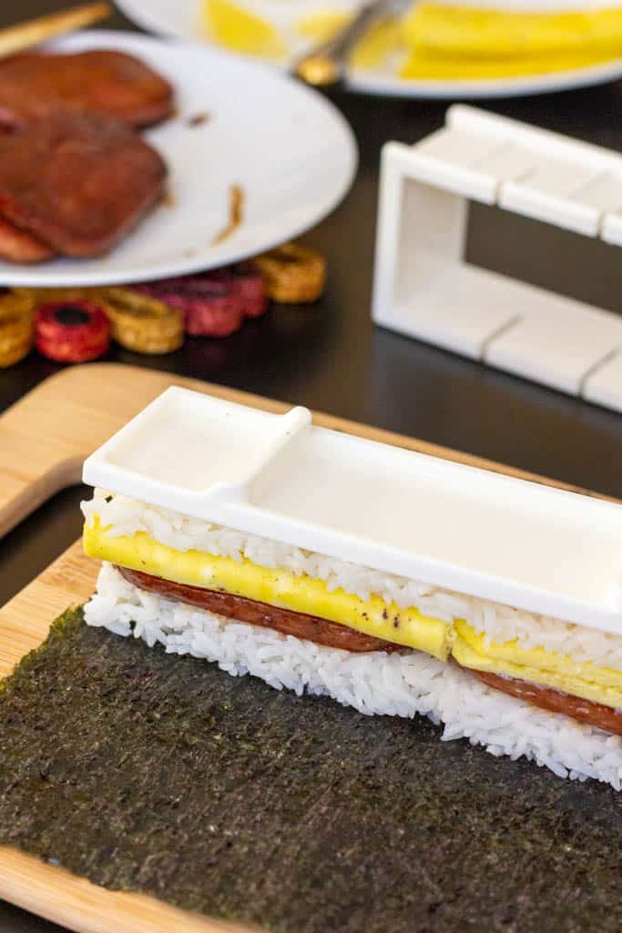 Step 7 of spam musubi with egg assembly: remove the outside of the mold from the rice, Spam and egg stack.