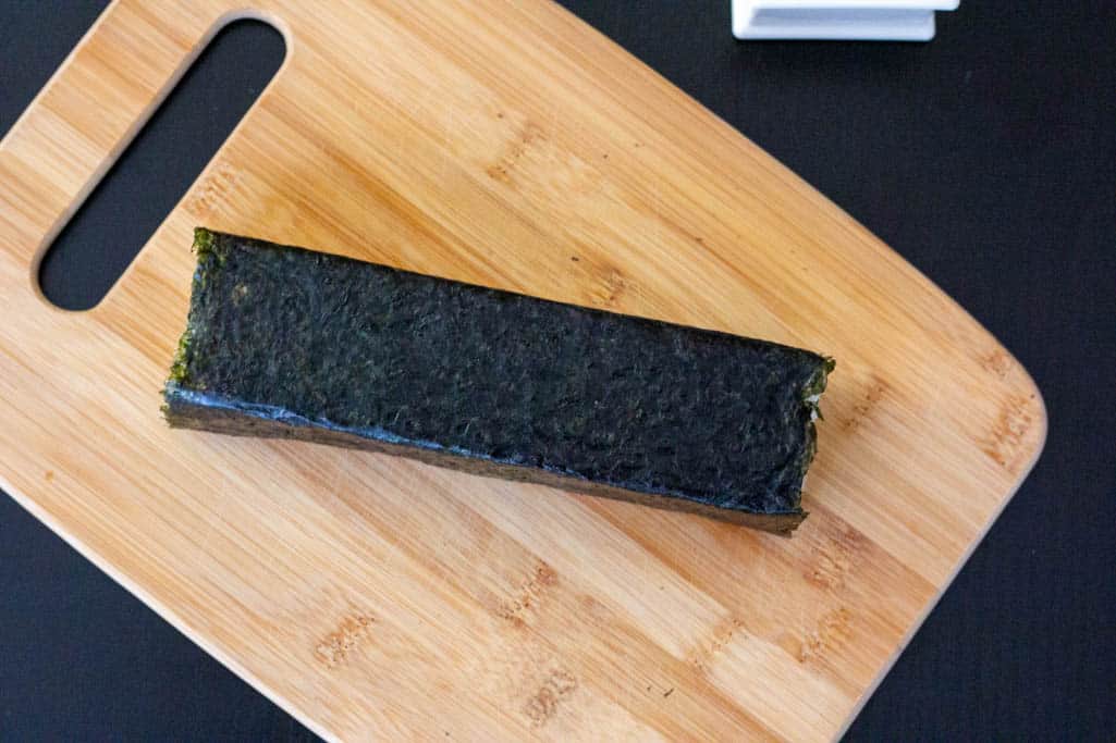 Step 8 of spam musubi with egg assembly: wrap the seaweed around the stack of rice, Spam and egg, and place seam side down.