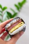 Hand holding a slice of spam musubi with egg.