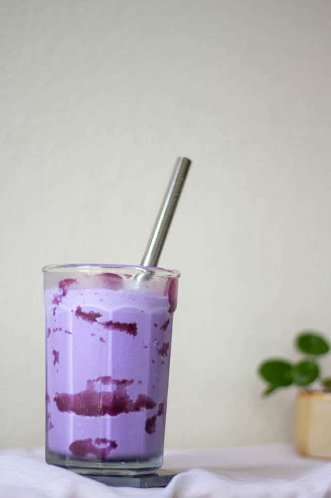 A large serving of bright purple ube milkshake in a tall clear cup, with a metal straw.