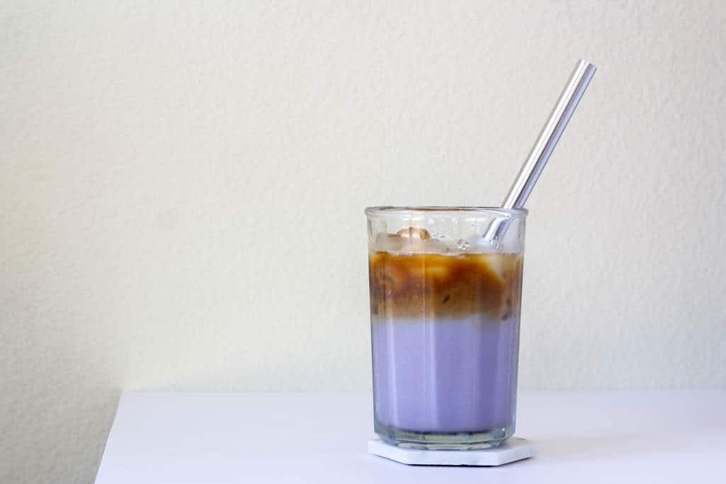 Iced ube latte topped with a shot of espresso, in a tall clear glass cup with a steel straw.