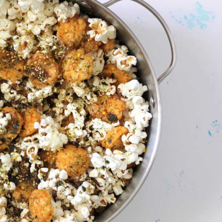 Pot full of popcorn topped with crispy golden brown crackers and dark green furikake.