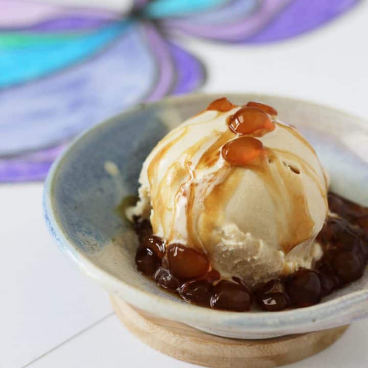 Small dish of beige, black tea flavored ice cream topped with semi opaque tapioca pearls bathed in brown sugar syrup.