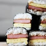 Stack of spam musubi with egg on a wooden cutting board.