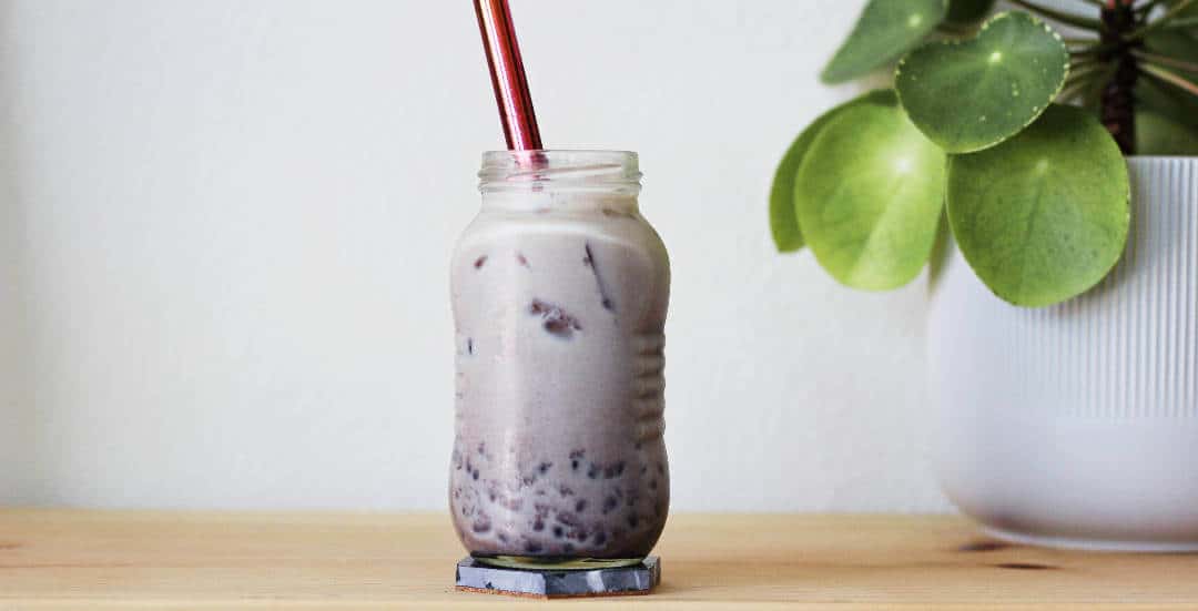 Clear jar filled with maroon-colored milk tea with bits of sweet red bean settling at the bottom of the jar.