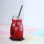 Clear glass filled with dark pink liquid and opaque white ice cubes floating in it.