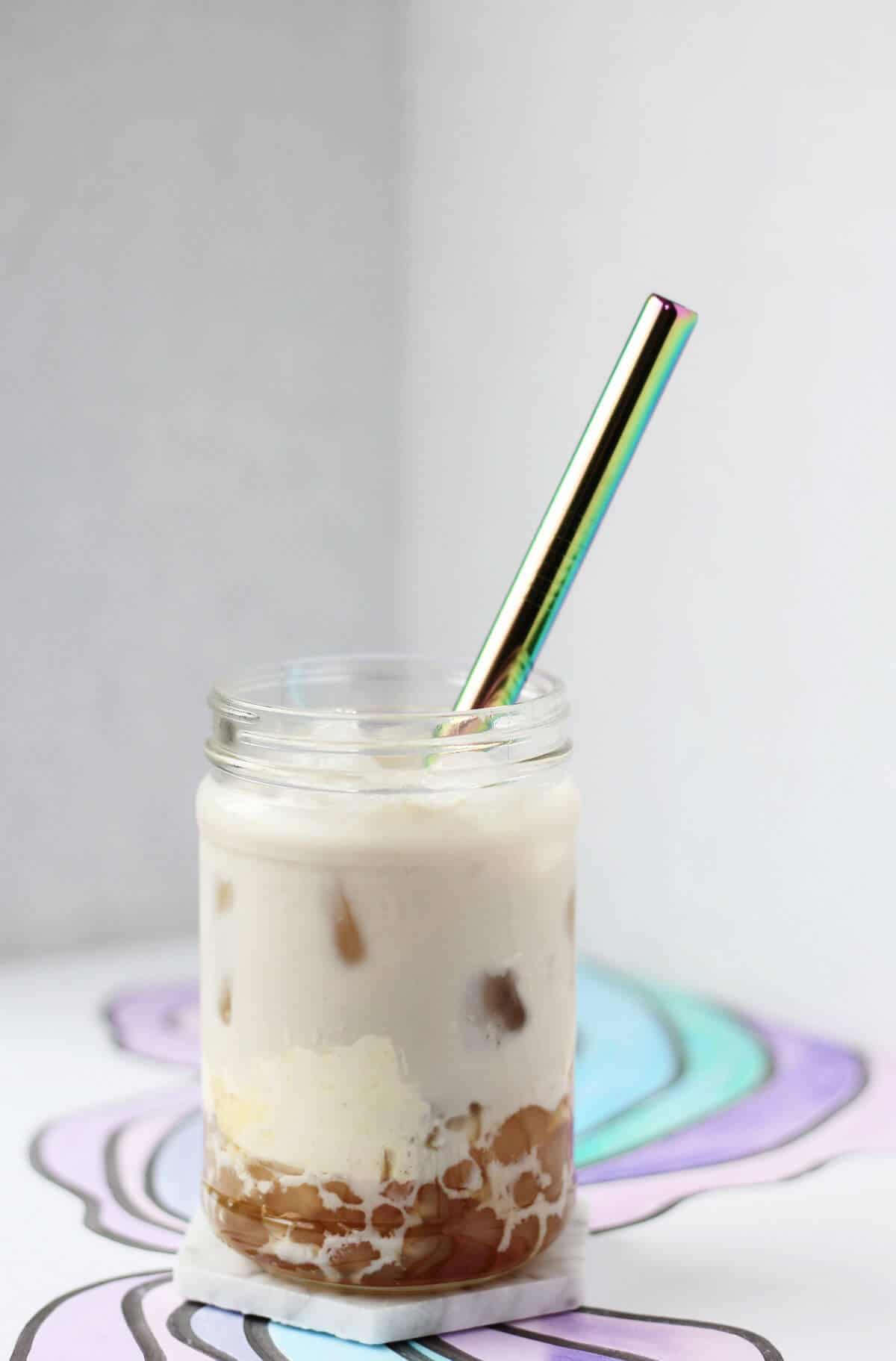 Clear glass filled with brown boba, crème brûlée custard, tan hojicha milk tea and ice.