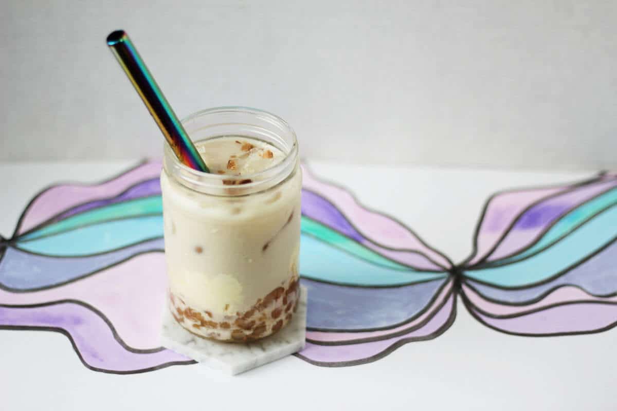 Clear jar with boba in brown sugar syrup, crème brûlée pudding and tan milk tea with ice and a metal straw.