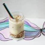 Clear glass jar with brown sugar boba, crème brûlée pudding, hojicha milk tea, ice and a metal straw.