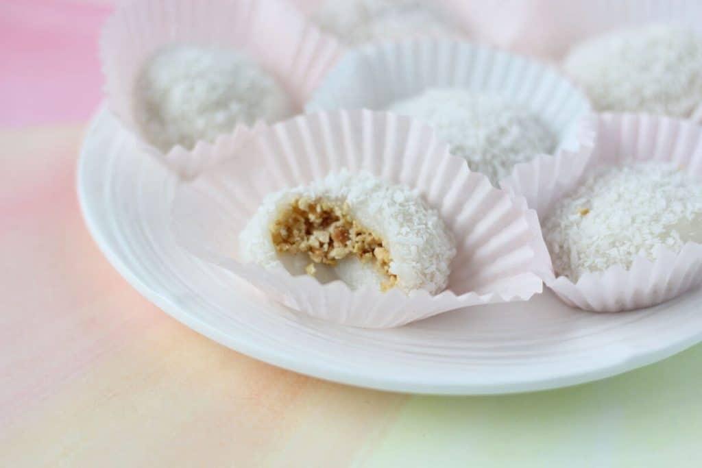 White ball of dough filled with golden brown chopped peanuts and dusted with coconut shreds.