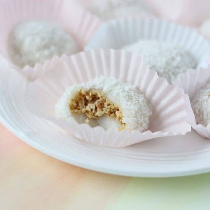 White dumpling coated in coconut shreds filled with chopped peanuts in a pink cupcake liner.