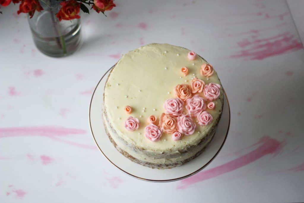 Top of a two layer cake frosted with white buttercream and decorated with pink frosting flowers.