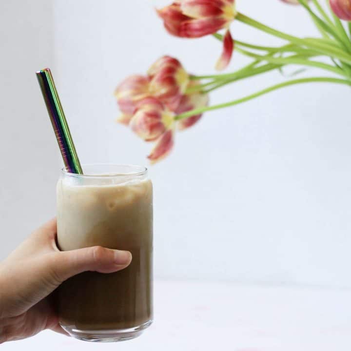Hand holding a clear cup of iced coffee with a metal straw.