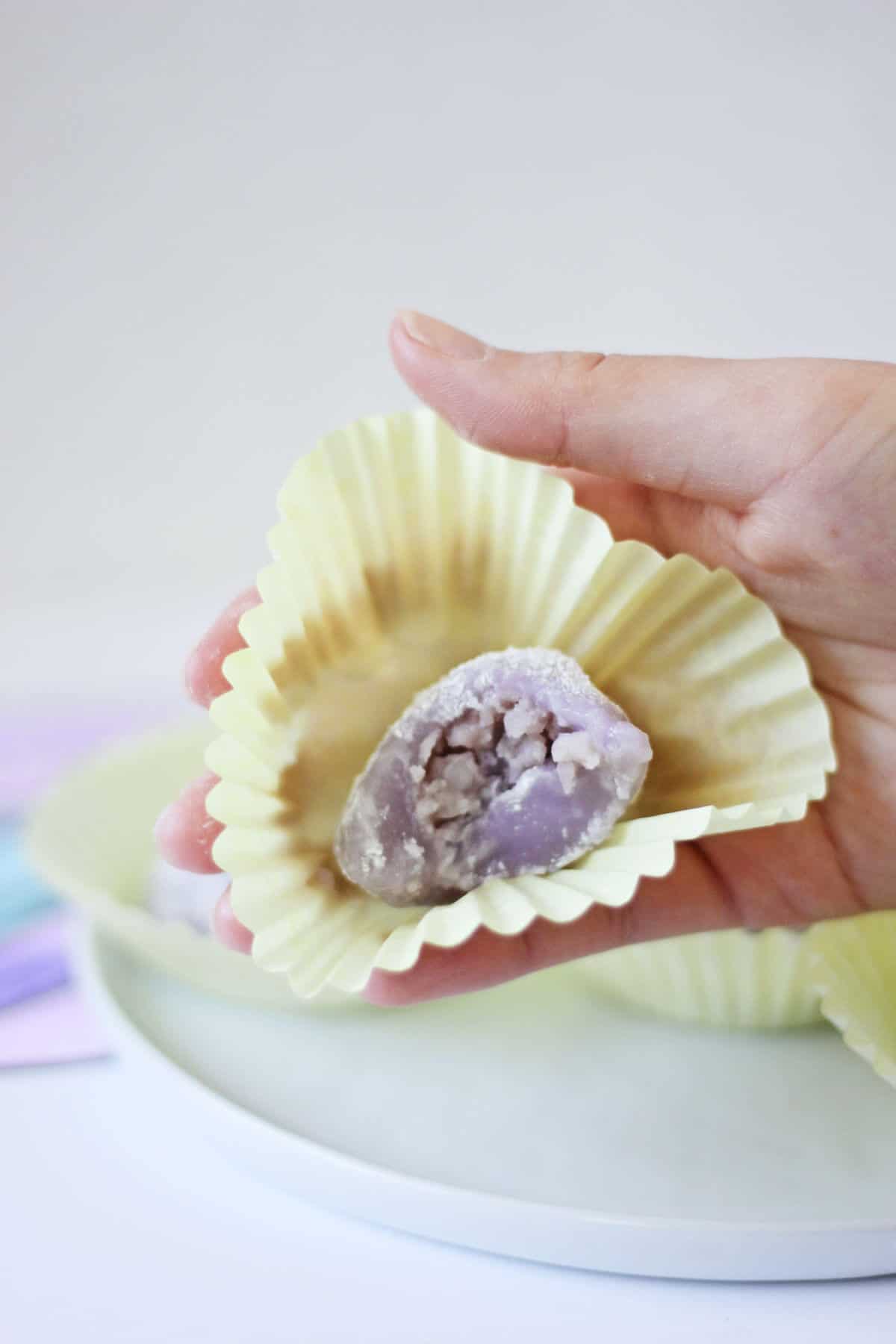 Hand holding a cupcake wrapper with a piece of purple mochi filled with mashed taro.