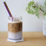 White coaster under clear glass with a layer of creamy lilac-colored taro milk topped with ice and a shot of espresso.