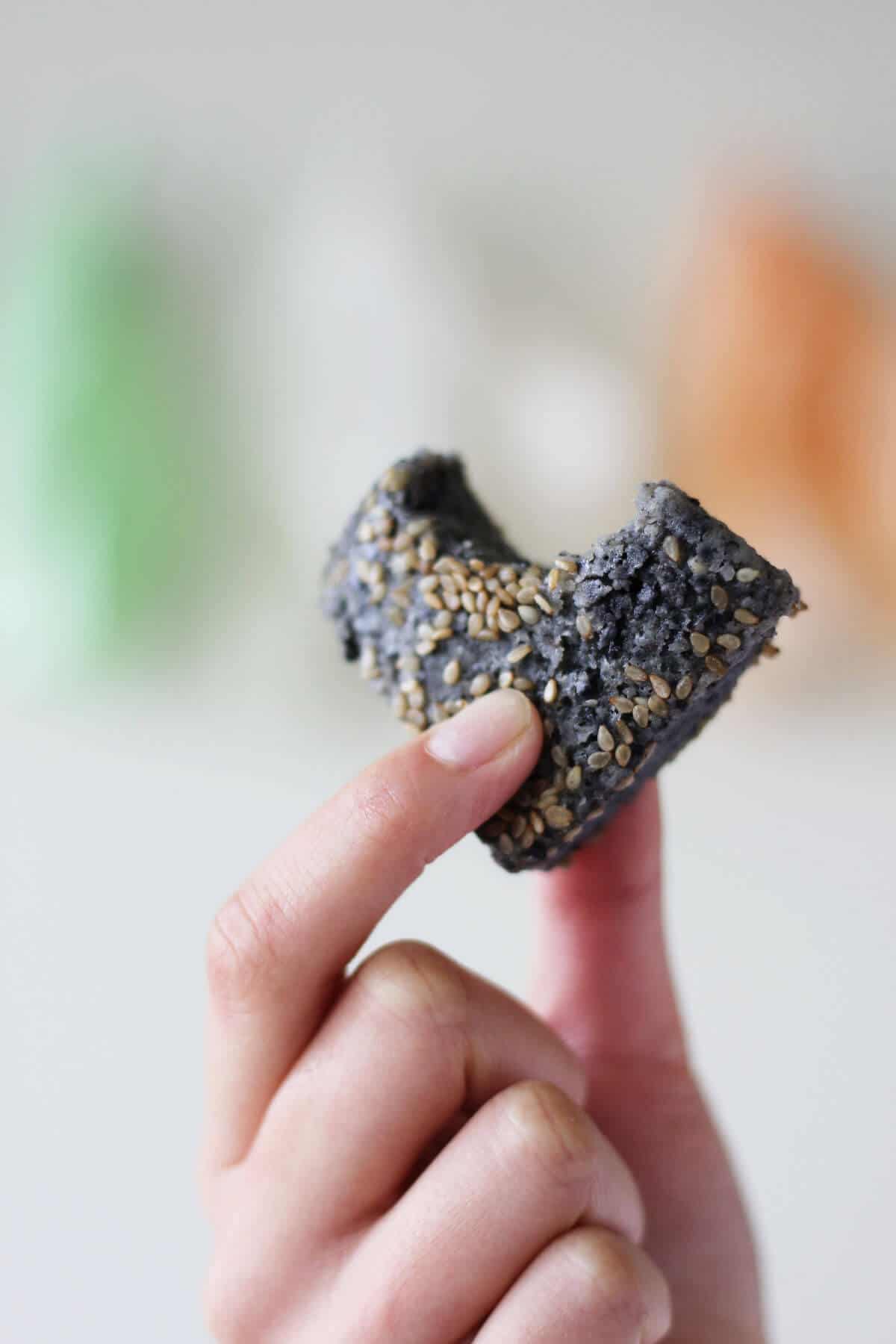 Hand holding square of black sesame mochi with a bite taken out of it.