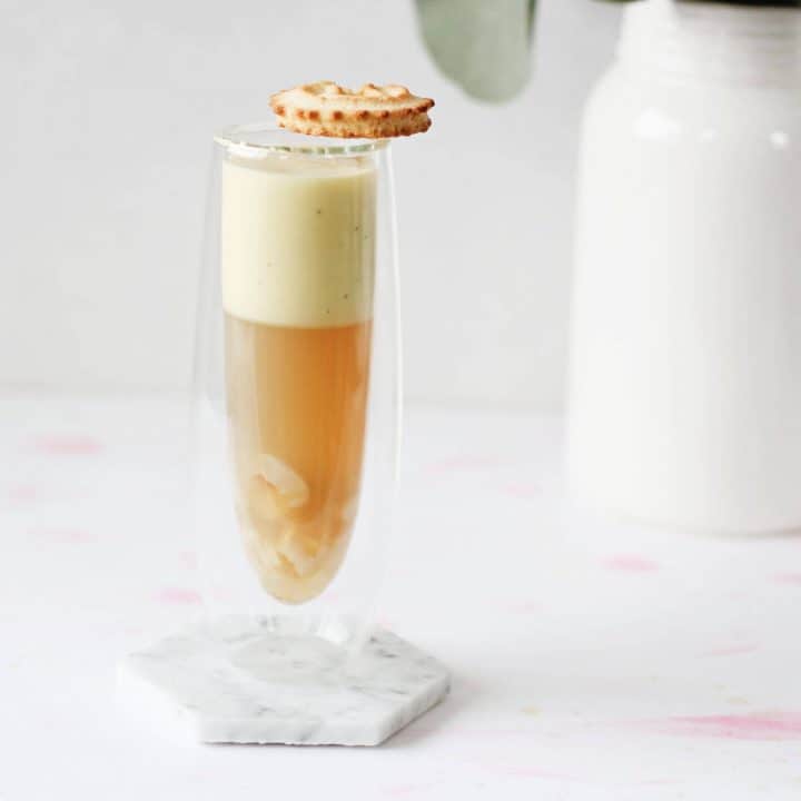 Clear champagne glass filled with orange/brown colored jelly and topped with beige coconut custard, with a cookie resting on the cup's rim.