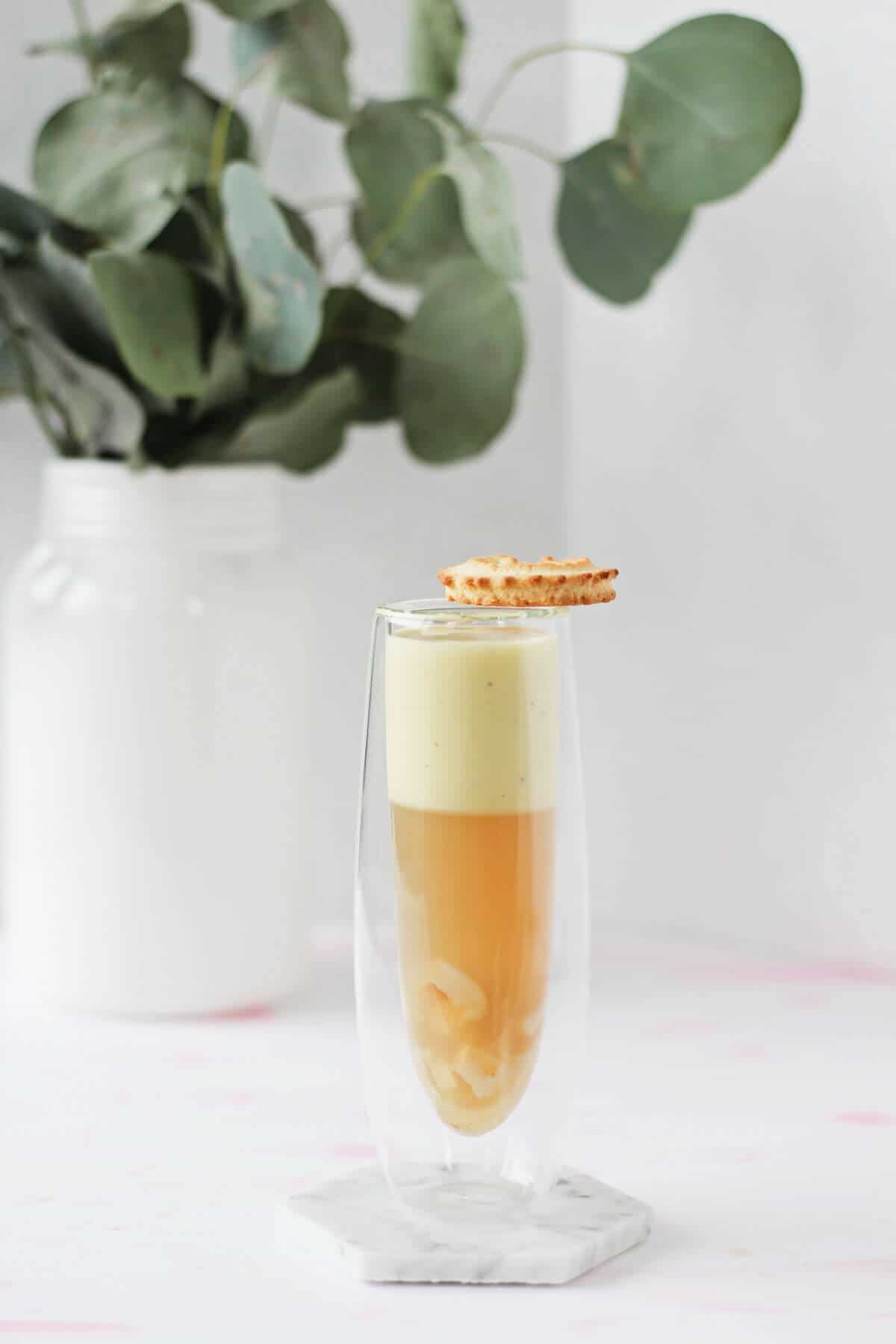 Clear champagne glass filled with orange-ish colored tea jelly mixed with chopped lychee, topped with off-white coconut custard and a crispy cookie.