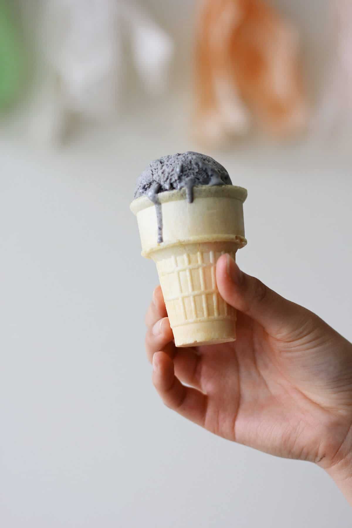Hand holding cone topped with dark grey colored ice cream scoop.
