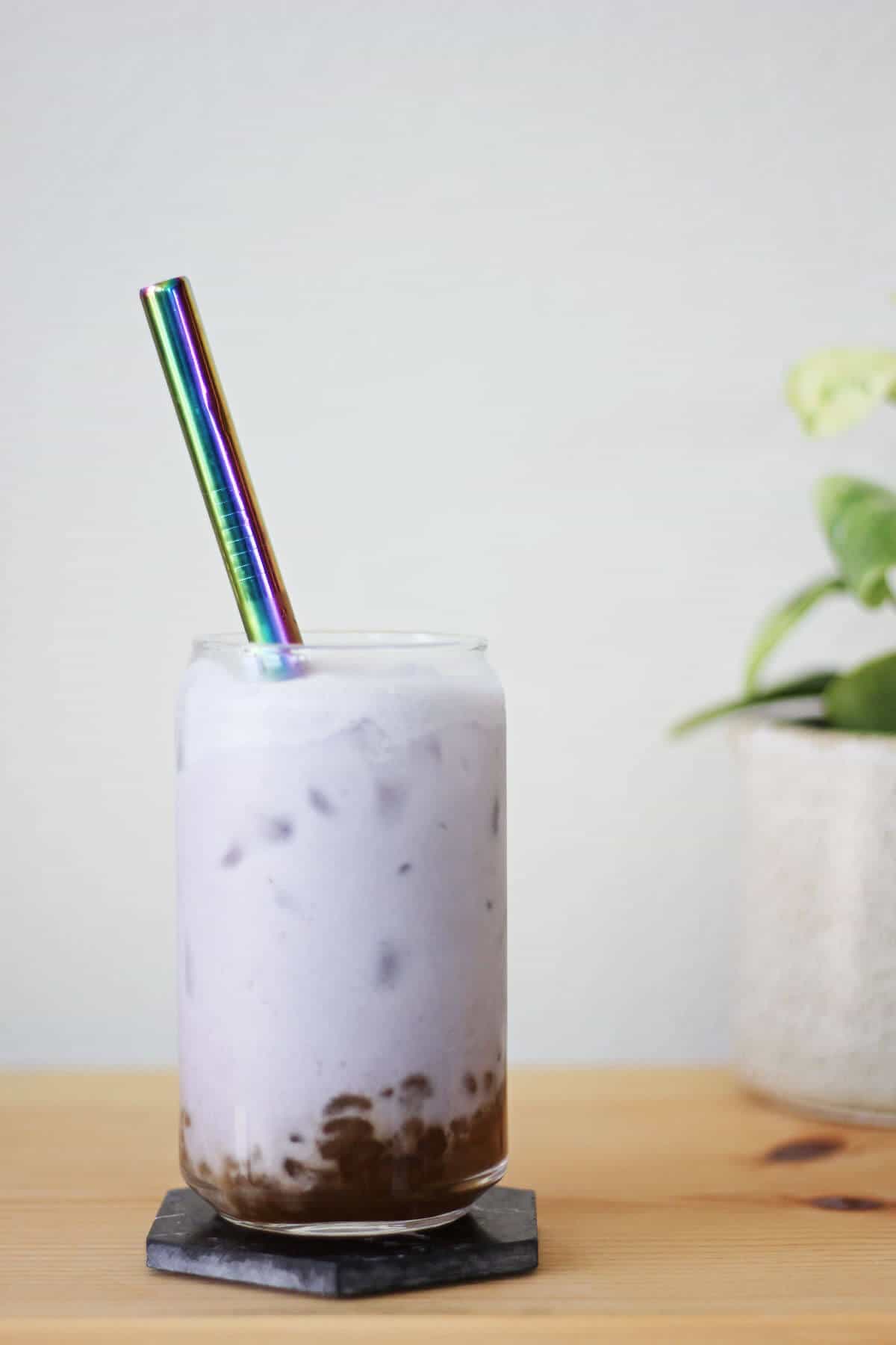 Clear glass filled with brown sugar boba, lilac milk tea, ice and a metal straw.