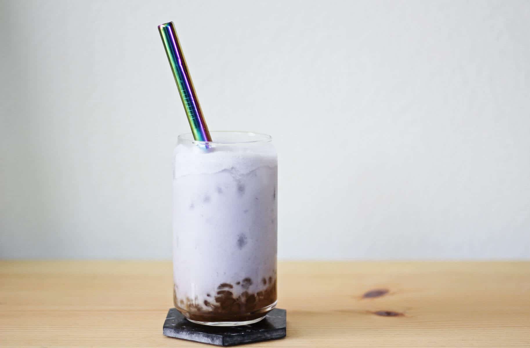 Clear glass filled with brown sugar boba, lilac milk tea, ice and a metal straw.