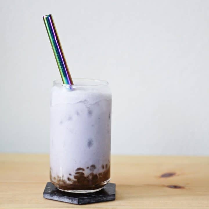 Clear glass filled with brown sugar boba and lilac colored taro milk tea and ice.