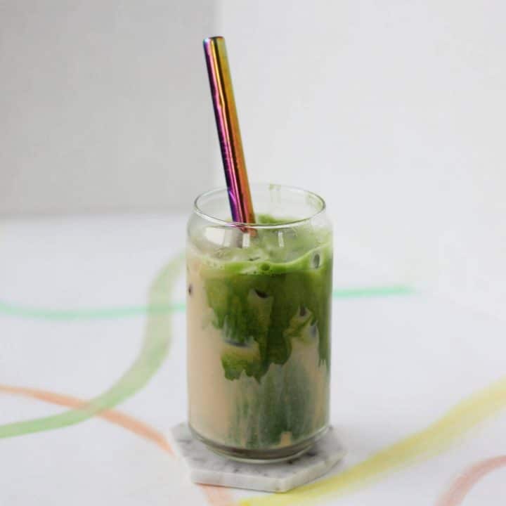 Clear glass filled with tan colored masala chai swirled with bright green matcha and a metal straw.