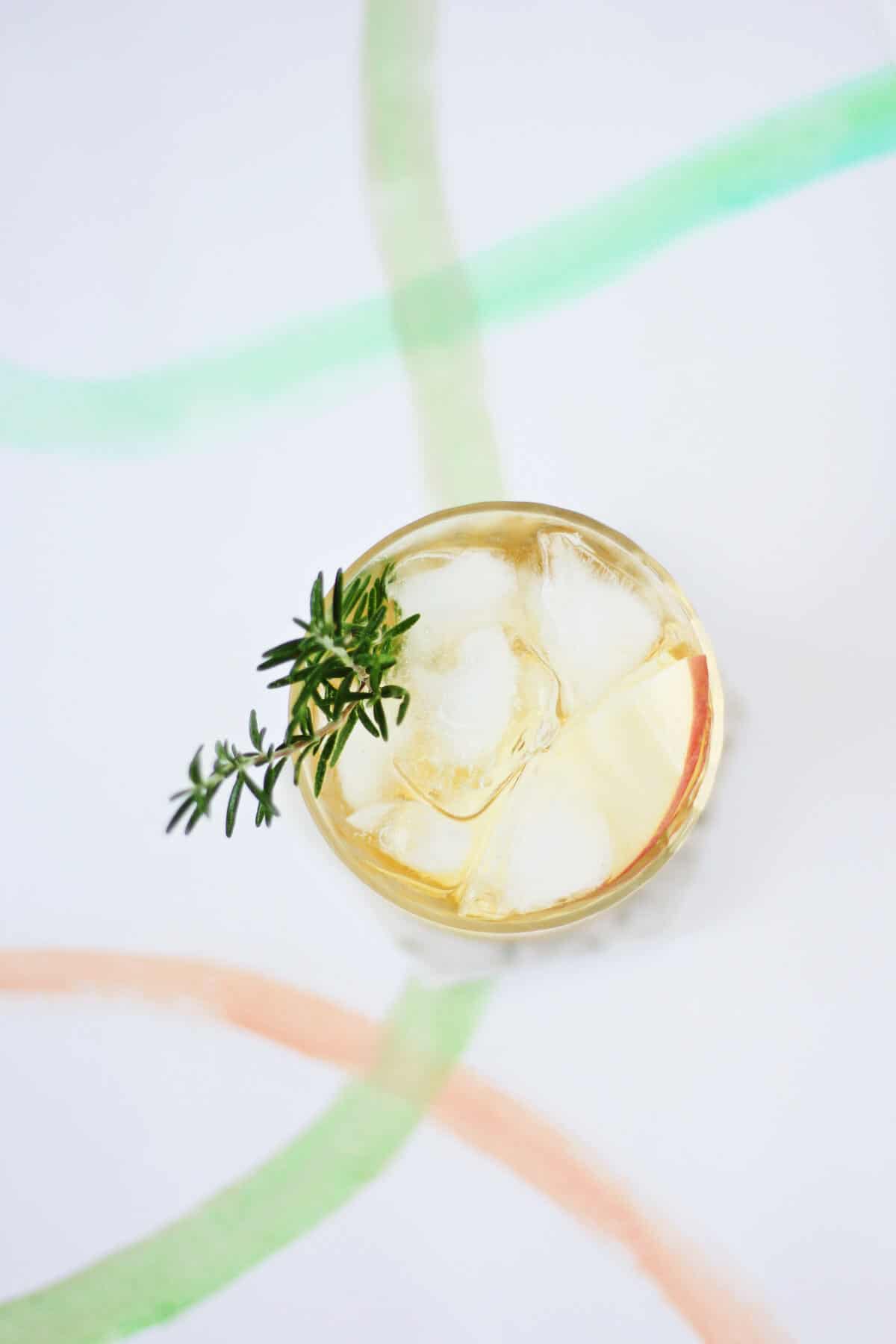 Overhead shot of yellow cocktail with ice cubes and a sprig of rosemary peeking out.
