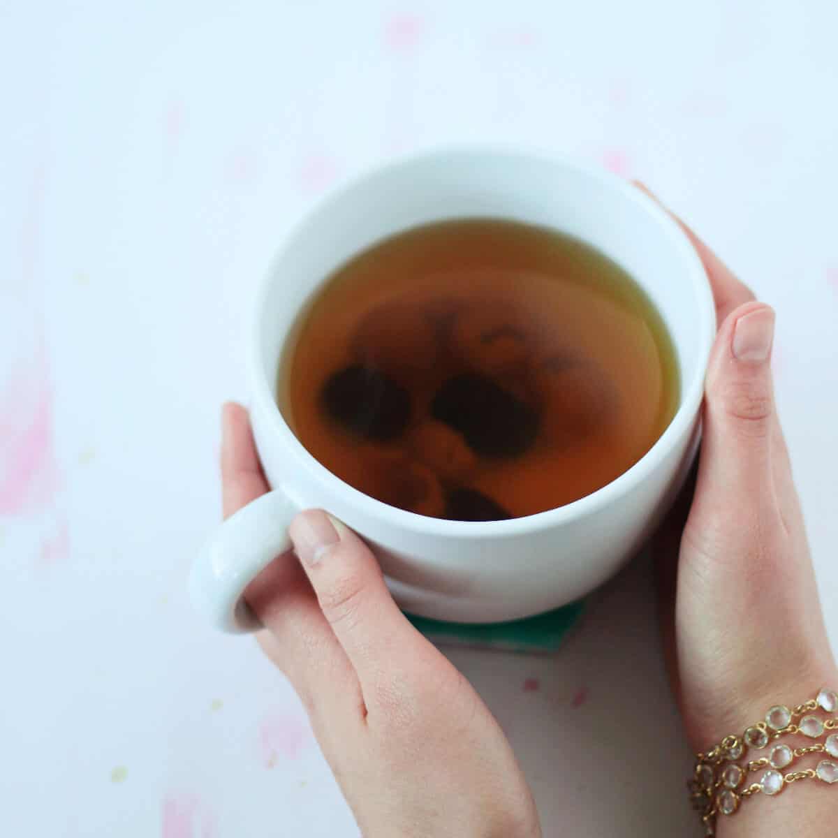 Hands cupping mug of reddish brown tea.