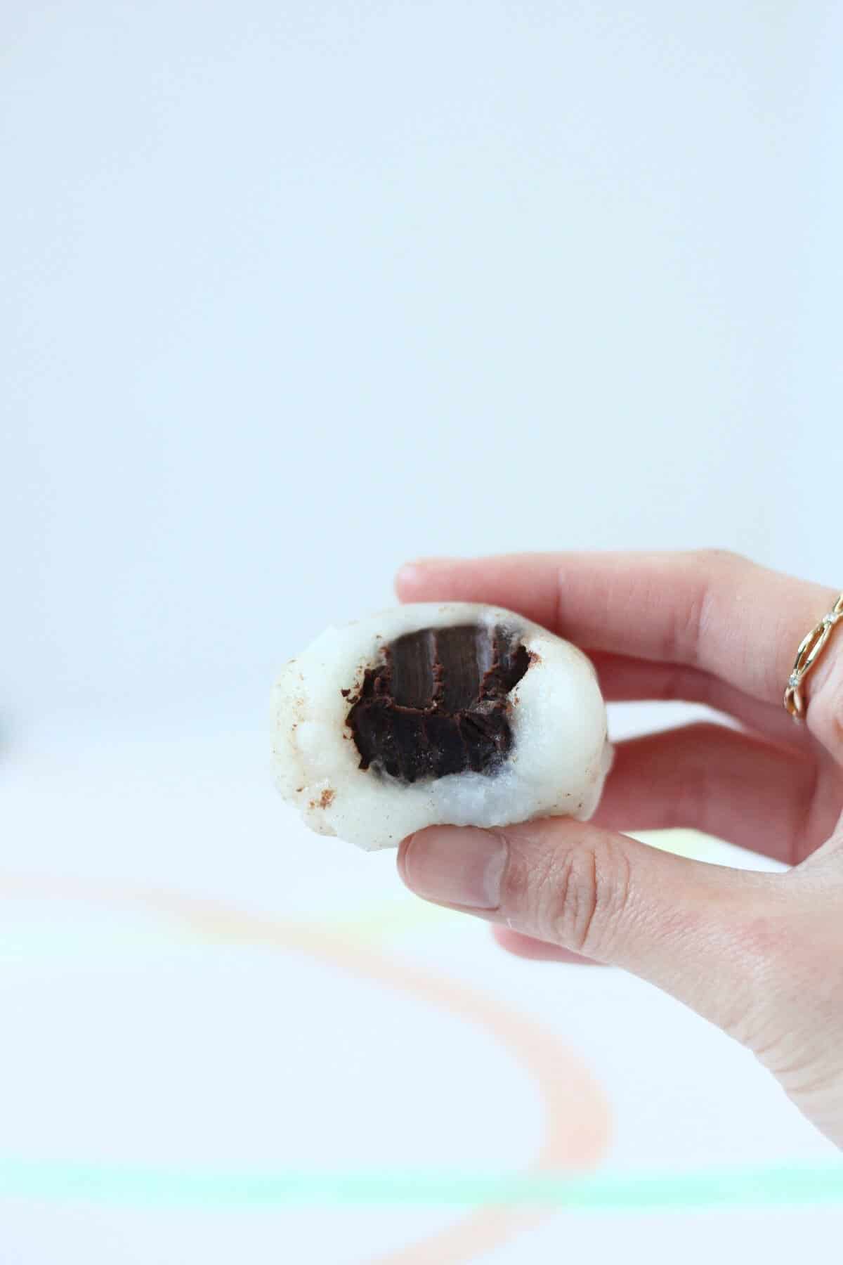 Hand holding bitten into white mochi filled with chocolate truffle.