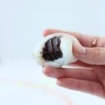 Hand holding bitten into white mochi filled with chocolate truffle.