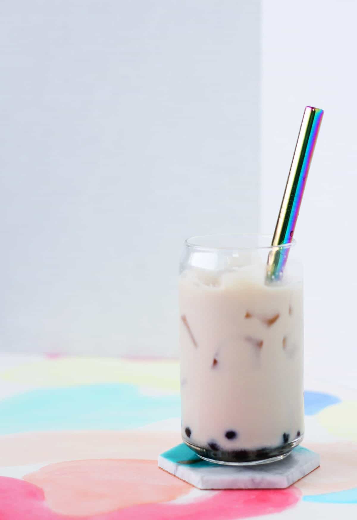 Clear glass cup filled with honey boba, ice and off white colored oolong milk tea with a metal straw.