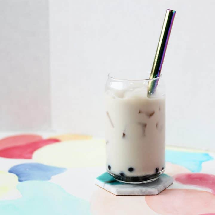 Clear glass cup filled with honey boba, ice and off white colored oolong milk tea with a metal straw.
