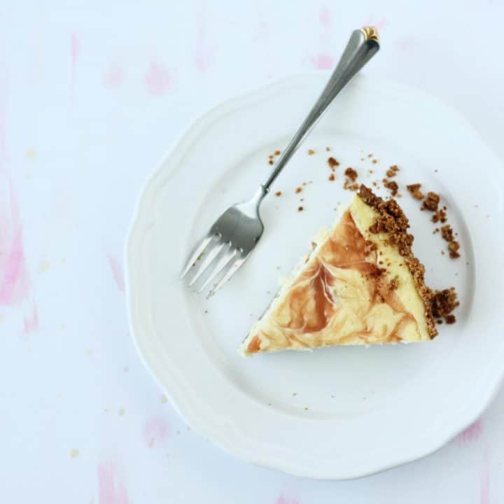 Slice of cheesecake with dark brown graham cracker crust and a swirl of pink guava jam on top!