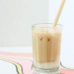 Clear glass filled with layer of white mochi, ice and creamy brown hued earl grey milk tea with a bamboo straw.