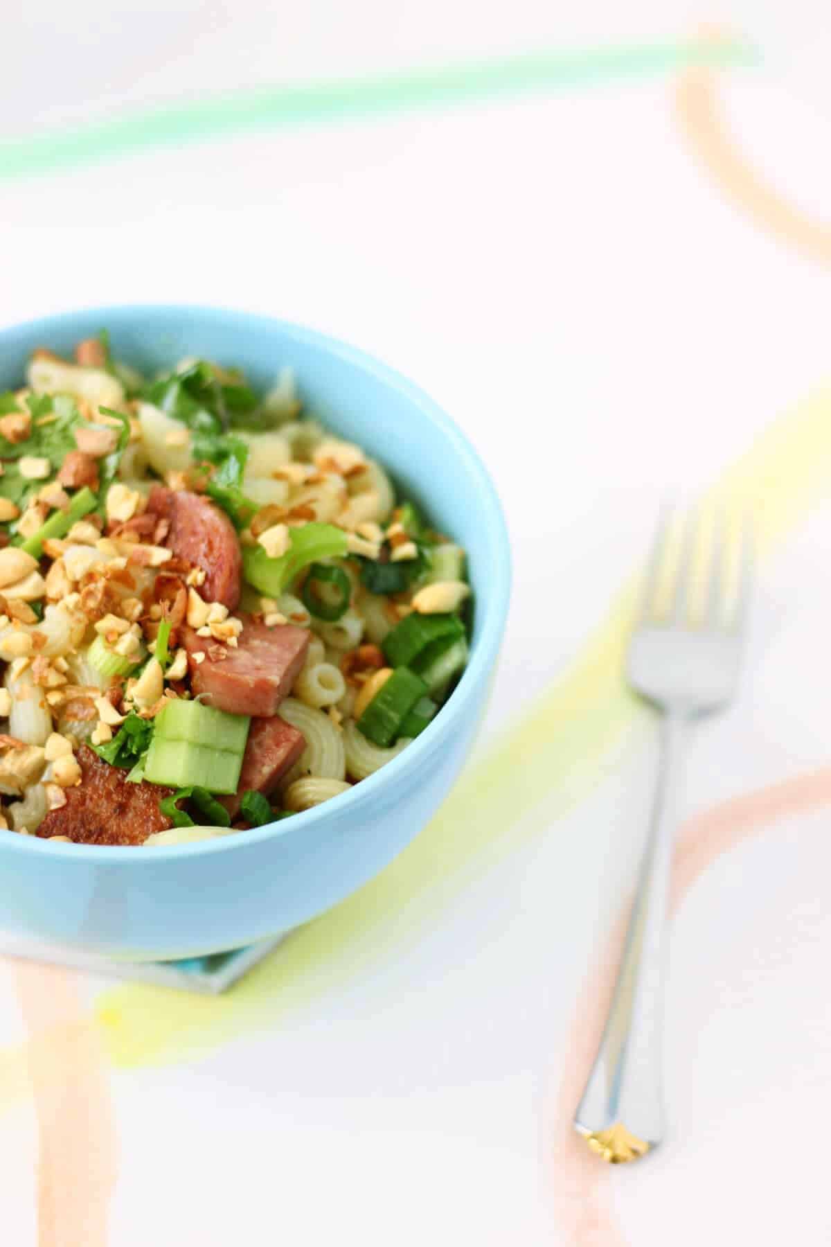 Pasta salad with chopped celery and chunks of spam in a light blue bowl.