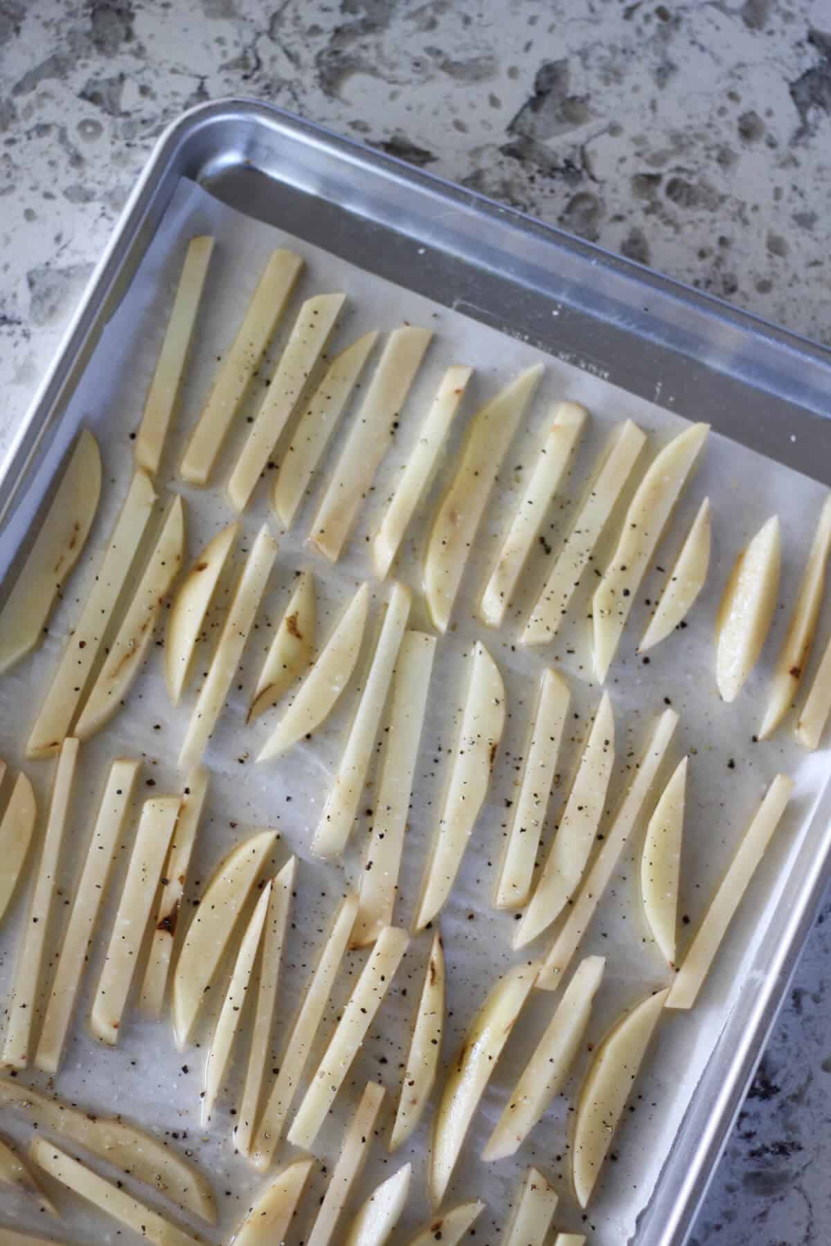 Raw potatoes cut into fries on a piece of parchment paper on a baking sheet.