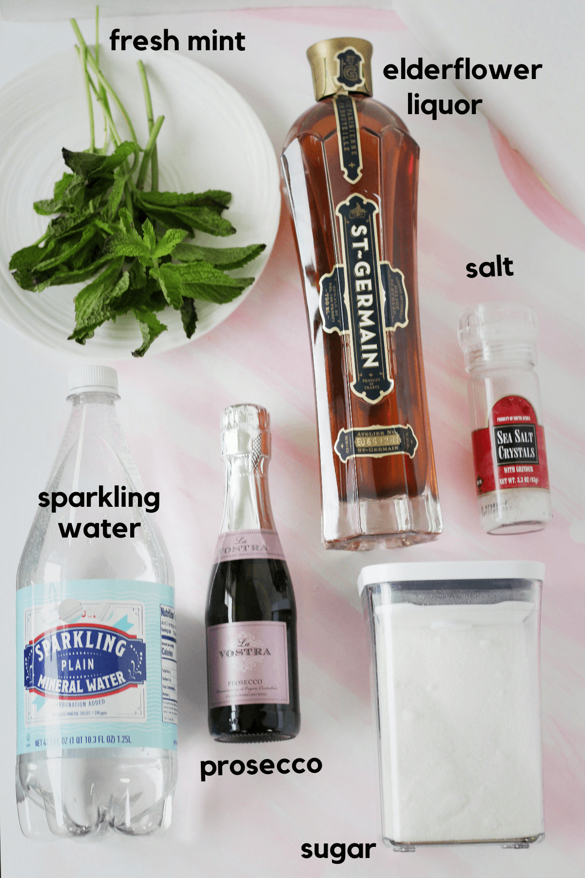 Ingredients laied out for a hugo spritz: sparkling water, prosecco, sugar, salt, elderflower liquor and fresh mint.
