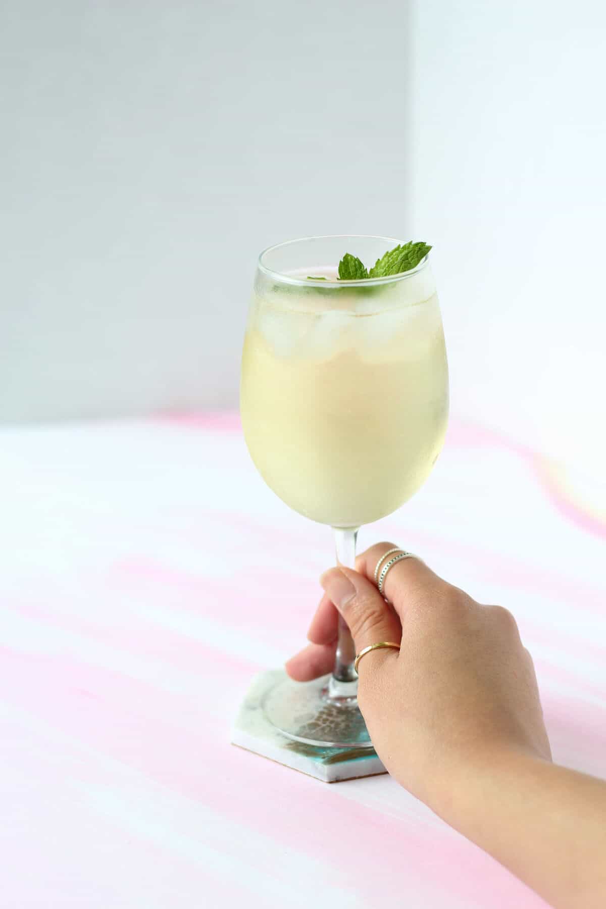 Head holding a wine glass filled with light yellow liquid and a sprig of mint on top.