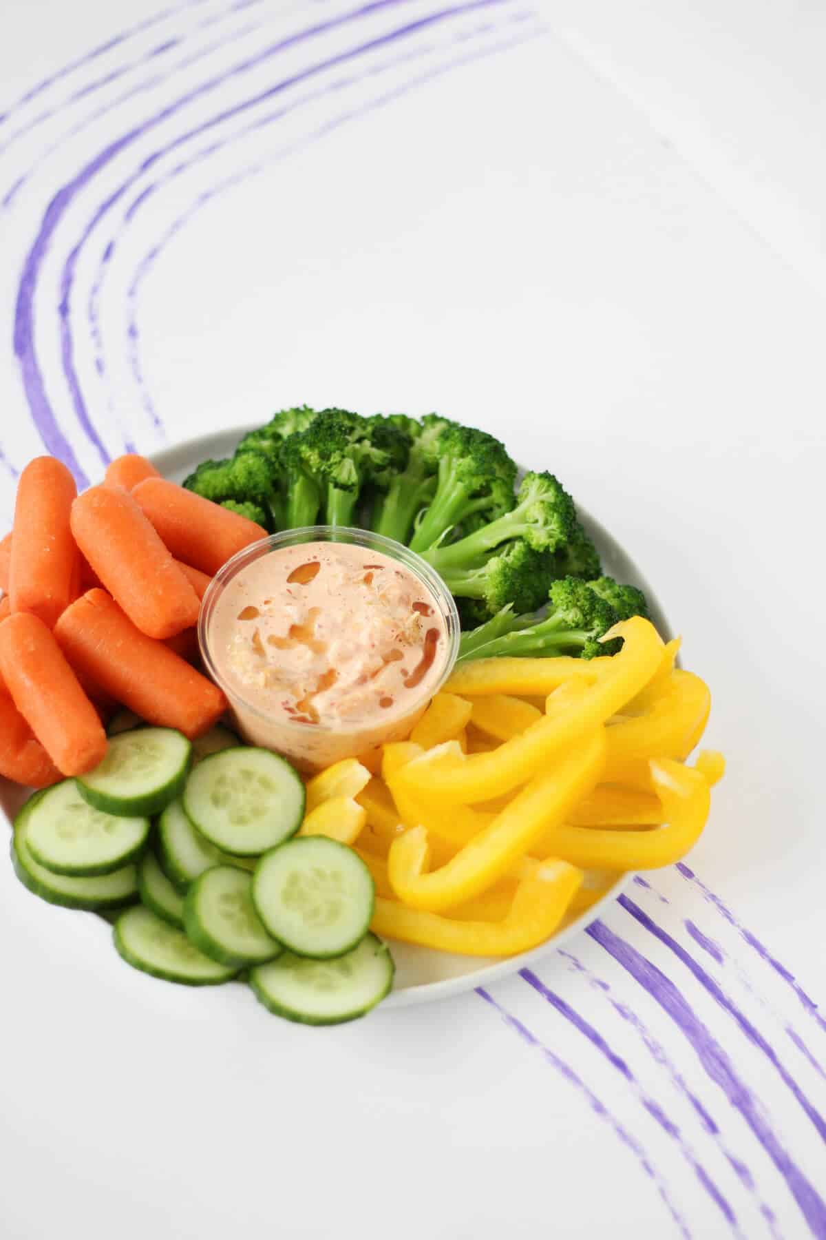A plate filled with vegetables (baby carrots, broccoli, bell pepper and cucumber) and a dish of orange-y kimchi mayo in the center.